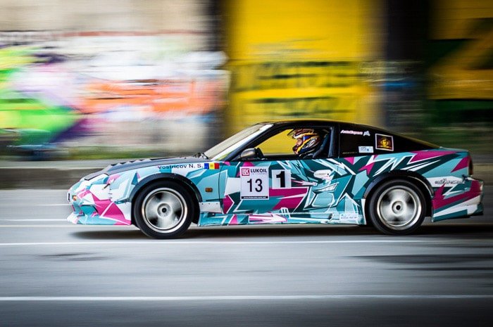 یک ماشین مسابقه‌ای رنگارنگ در حال رانندگی با پس زمینه تاری حرکت