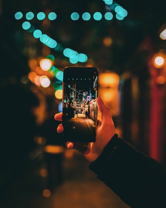 دستی که یک تلفن هوشمند را در دست دارد تا به طور طبیعی یک عکس خیابانی شب را قاب بگیرد ، با استفاده از عمق میدان گسترده و کم عمق