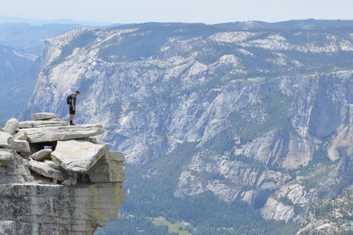 مردی که روی لبه صخره ایستاده با چشم انداز کوهستانی چشمگیر پشت سرش که تعادل وزن اندازه را در عکاسی نشان می دهد