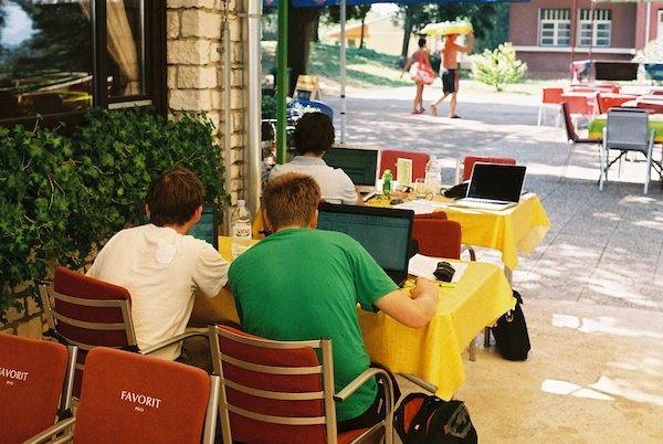  3 جوان پشت به ما در کافه ای هستند و با لپ تاپ هایشان کار می کنند.