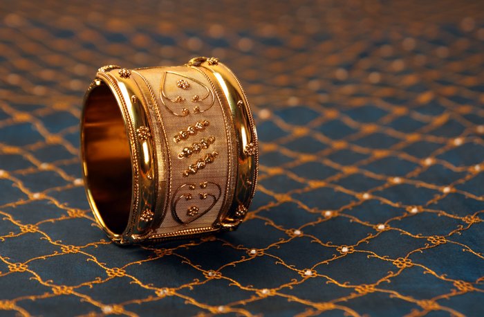 یک دستبند طلا روی پارچه آبی و طلایی