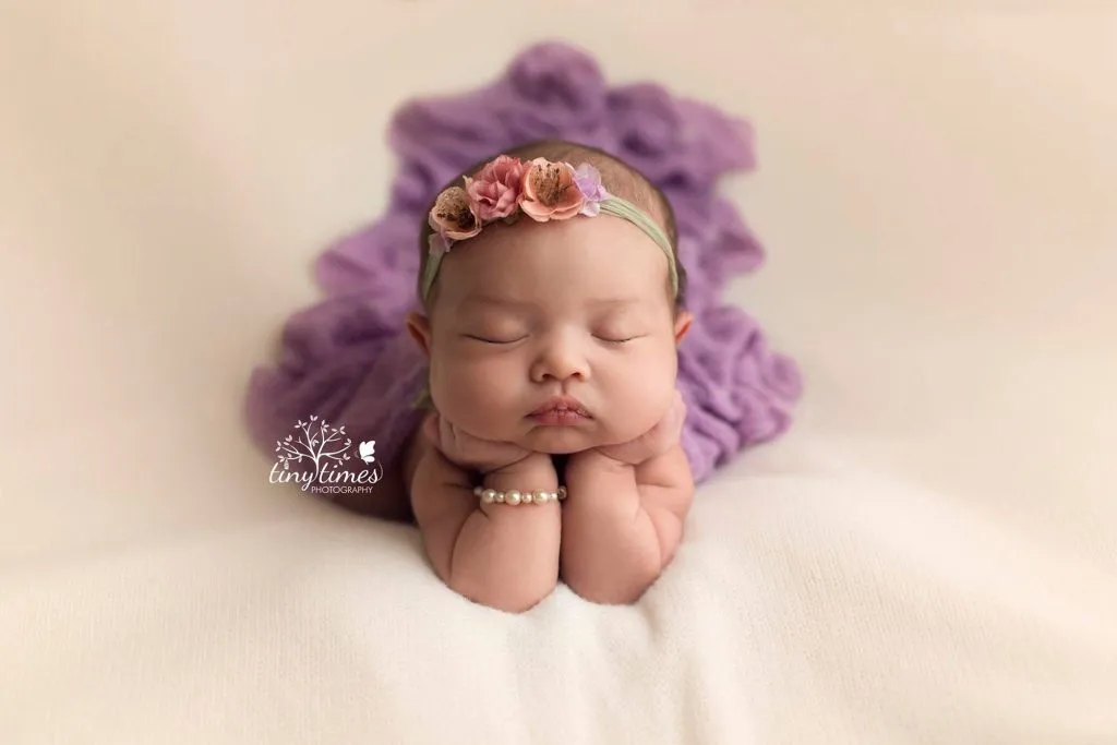 نوزاد خوابیده با هدبند گلدار و دکوراسیون بنفش در عکاسی حرفهای