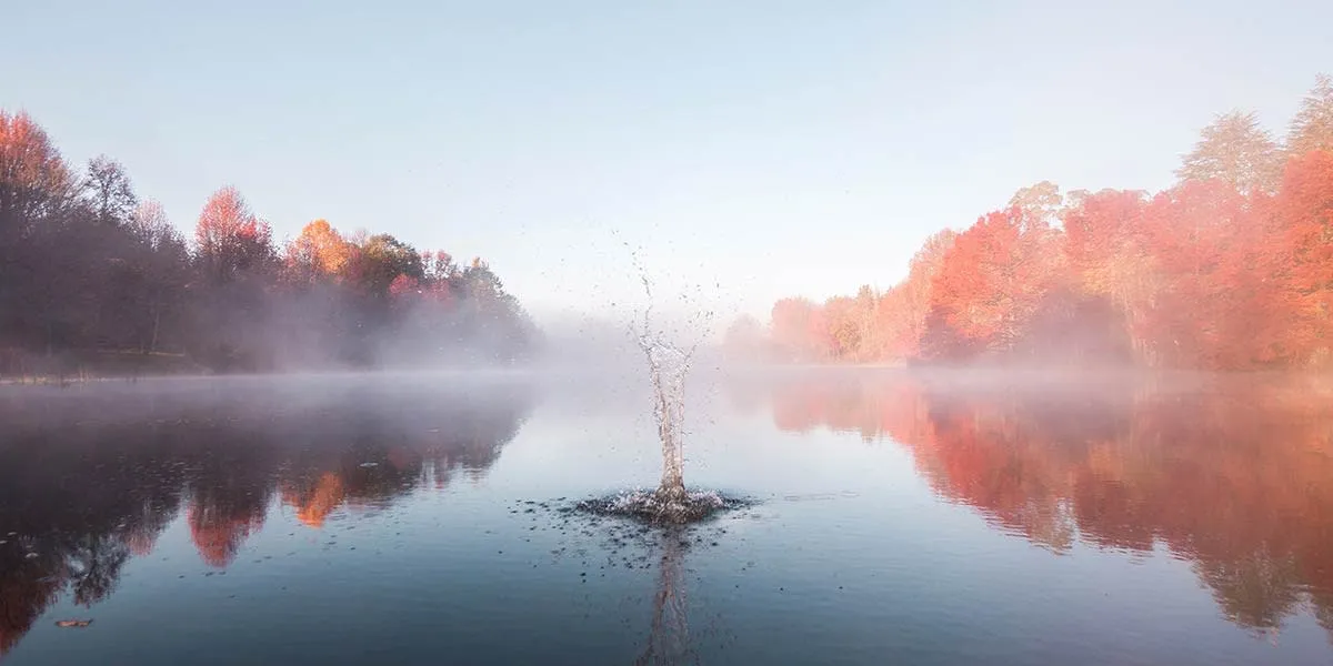 rock splashing in a lake with fog in the background