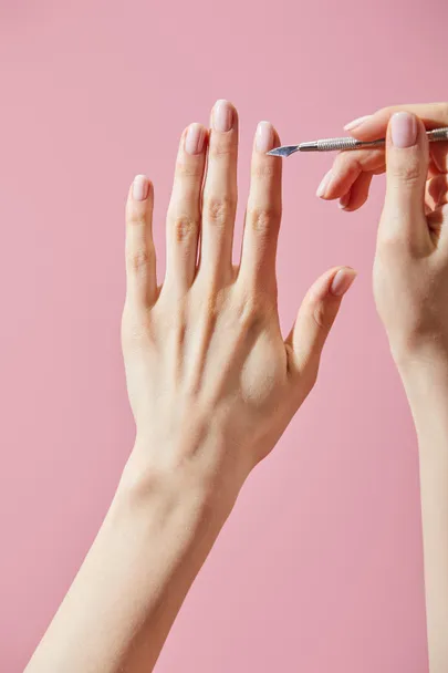 stock photo partial view woman doing manicure cuticle pusher isolated pink