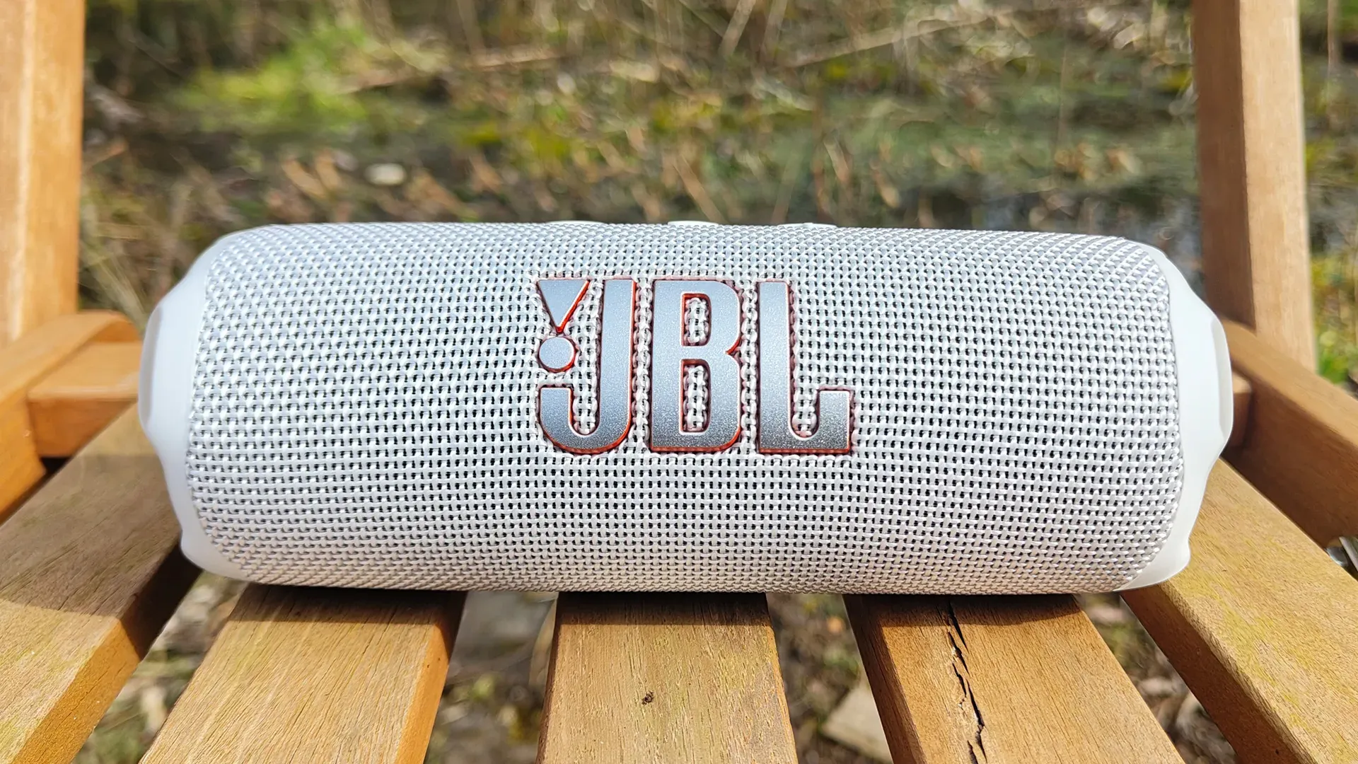اسپیکر JBL Flip 7 سفید با نمای روبهرو روی صندلی چوبی در طبیعت