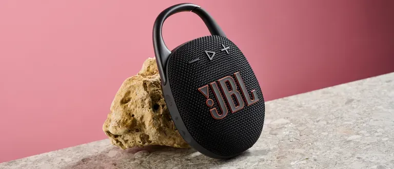اسپیکر JBL Clip 5 مشکی در حال تکیه دادن به سنگ با بکگراند صورتی تیره