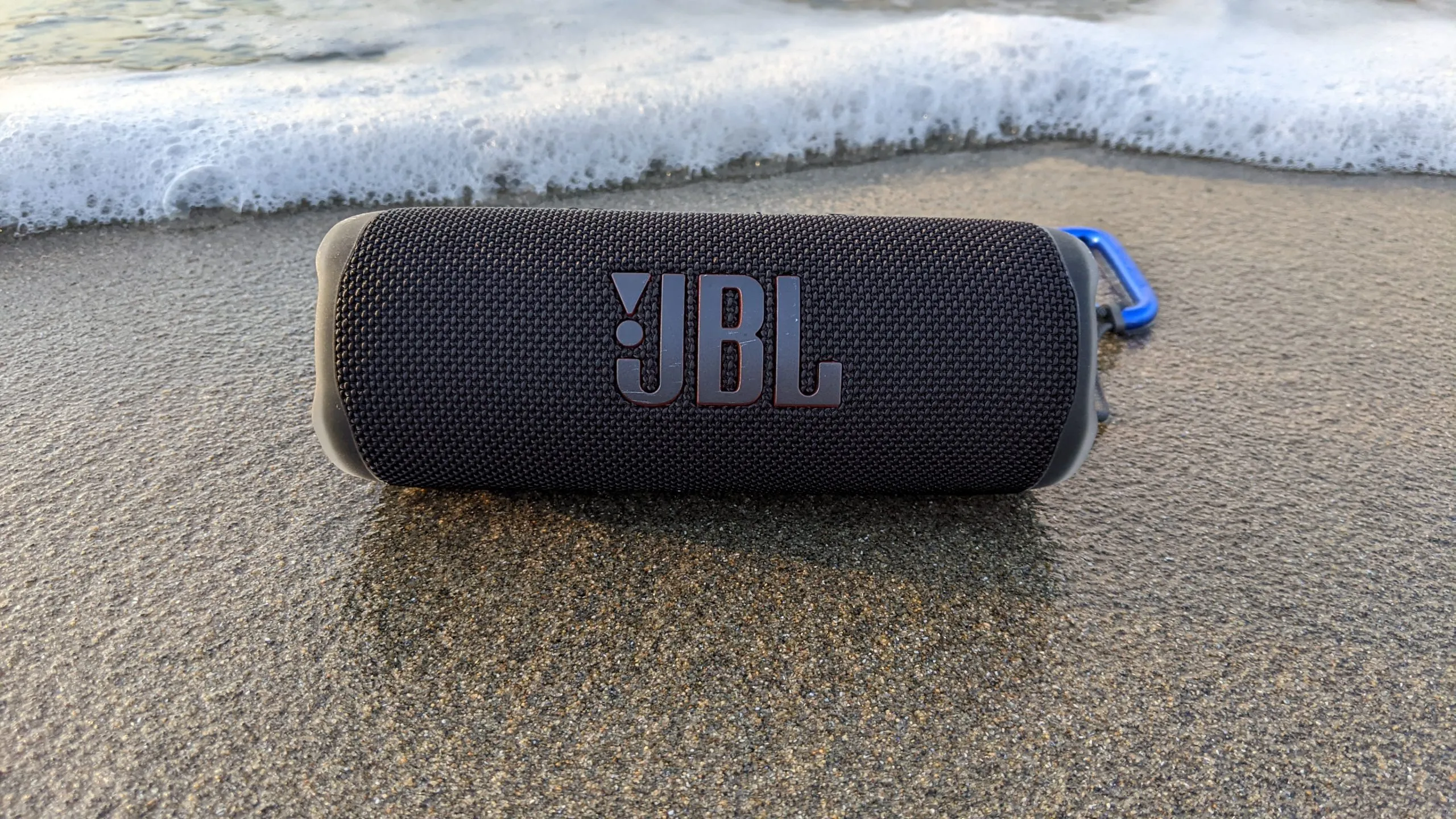 اسپیکر JBL Flip 6 در فضای باز روی شنهای ساحل، مناسب برای مهمانی و طبیعتگردی