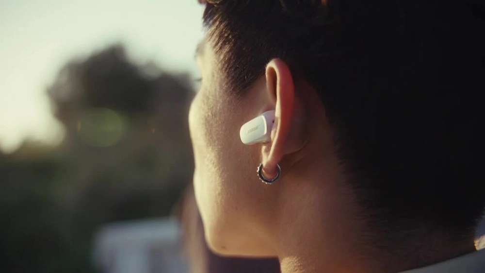 تصویر فردی در فضای باز که هدفون سفید Bose QuietComfort Earbuds II در گوش دارد؛ طراحی جمعوجور و فیت دقیق در گوش مشخص است.