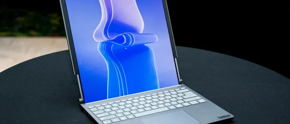 لپ‌تاپ Lenovo ThinkPad نقره‌ای با صفحه‌نمایش روشن روی میز گرد مشکی.